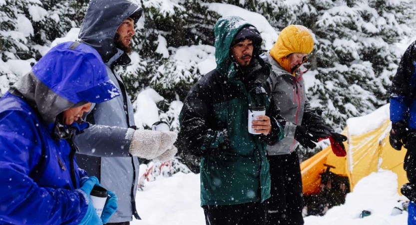 a group of veterans wearing snow gear drink hot drinks at their campsite